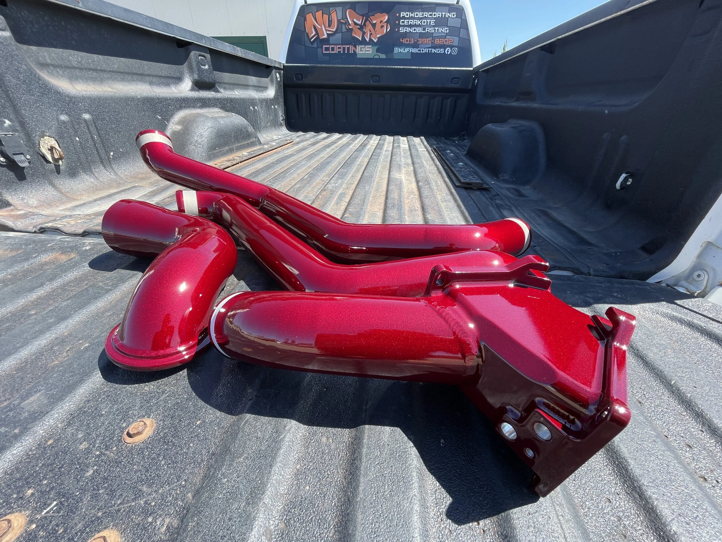 Red automotive exhaust headers placed on the bed of a pickup truck with a sign in the background advertising coating services.