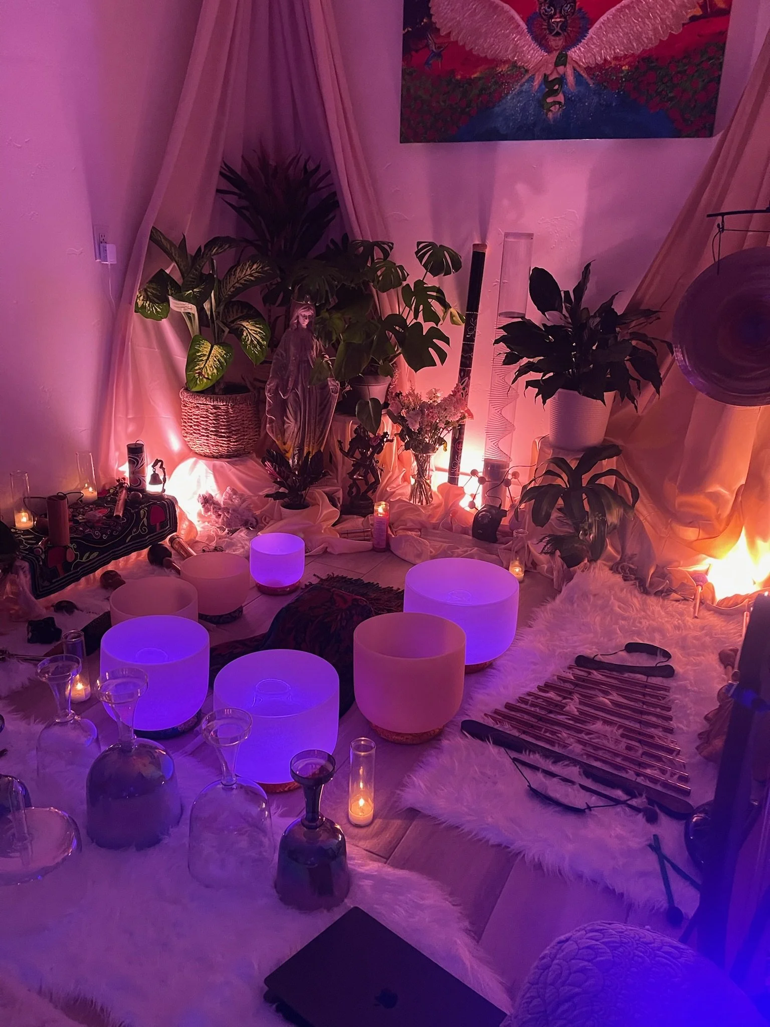 Cozy meditation or music space featuring glowing purple and pink lights, crystal bowls, candles, plants, and spiritual decor on a furry rug.