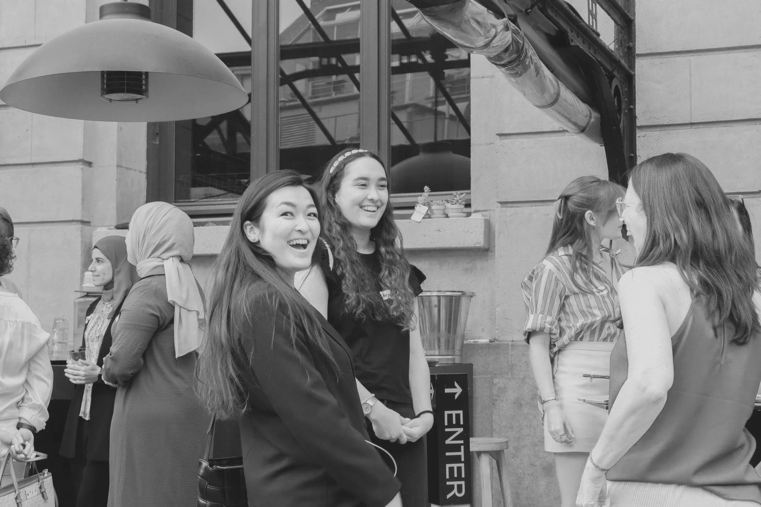 A group of women standing and chatting outside a building, smiling and laughing.