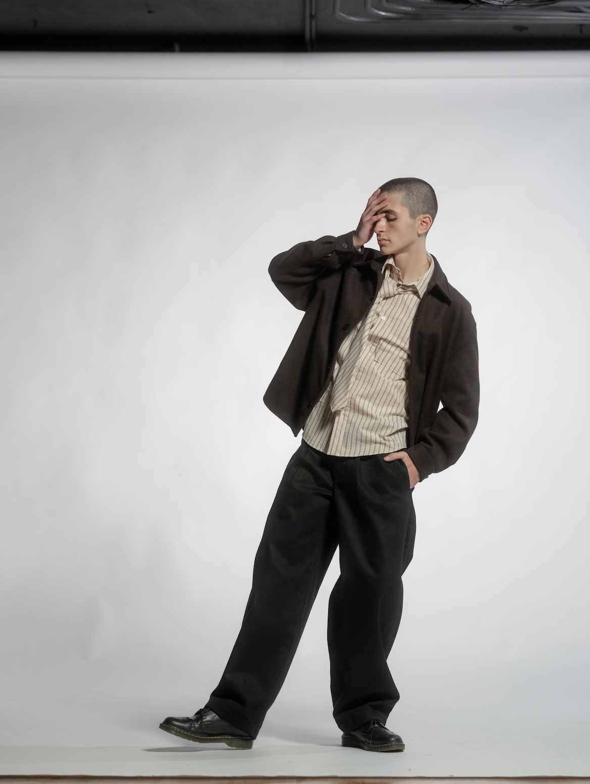 Young man with short hair in casual attire, holding his forehead in distress, standing against a plain white background.