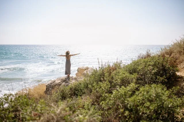 woman on the coast arms stretched triumphantly