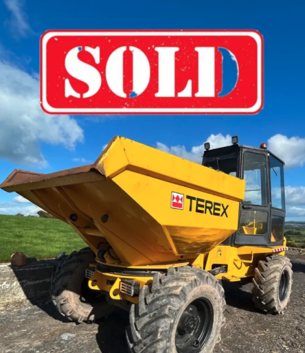 Yellow Terex front loader with a red 'Sold' sign above it, on a grassy field under a partly cloudy blue sky.