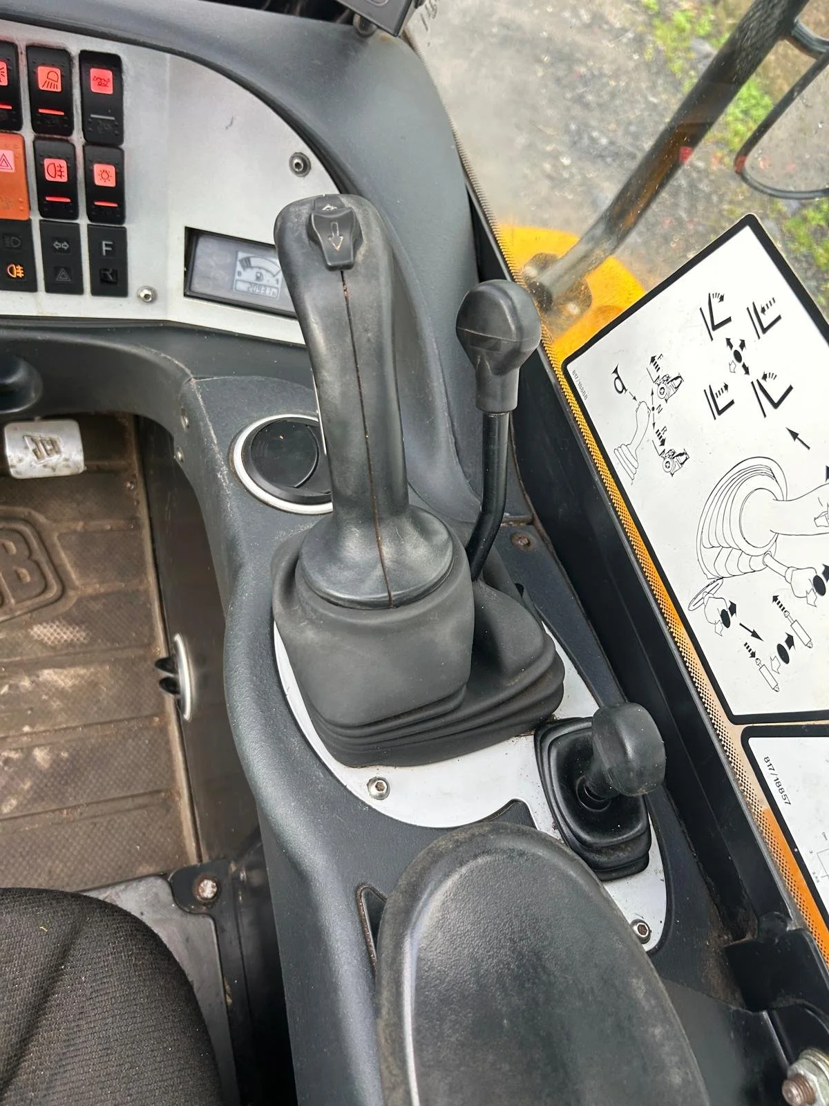 Interior view of construction equipment controls featuring two levers, a control panel with buttons, and an instruction diagram on the dashboard