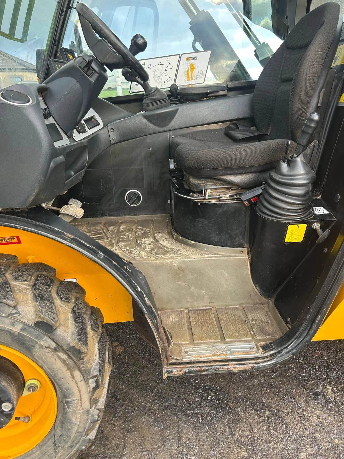 Interior view of a construction vehicle showing the driver's seat, steering wheel, control levers, and foot pedal.
