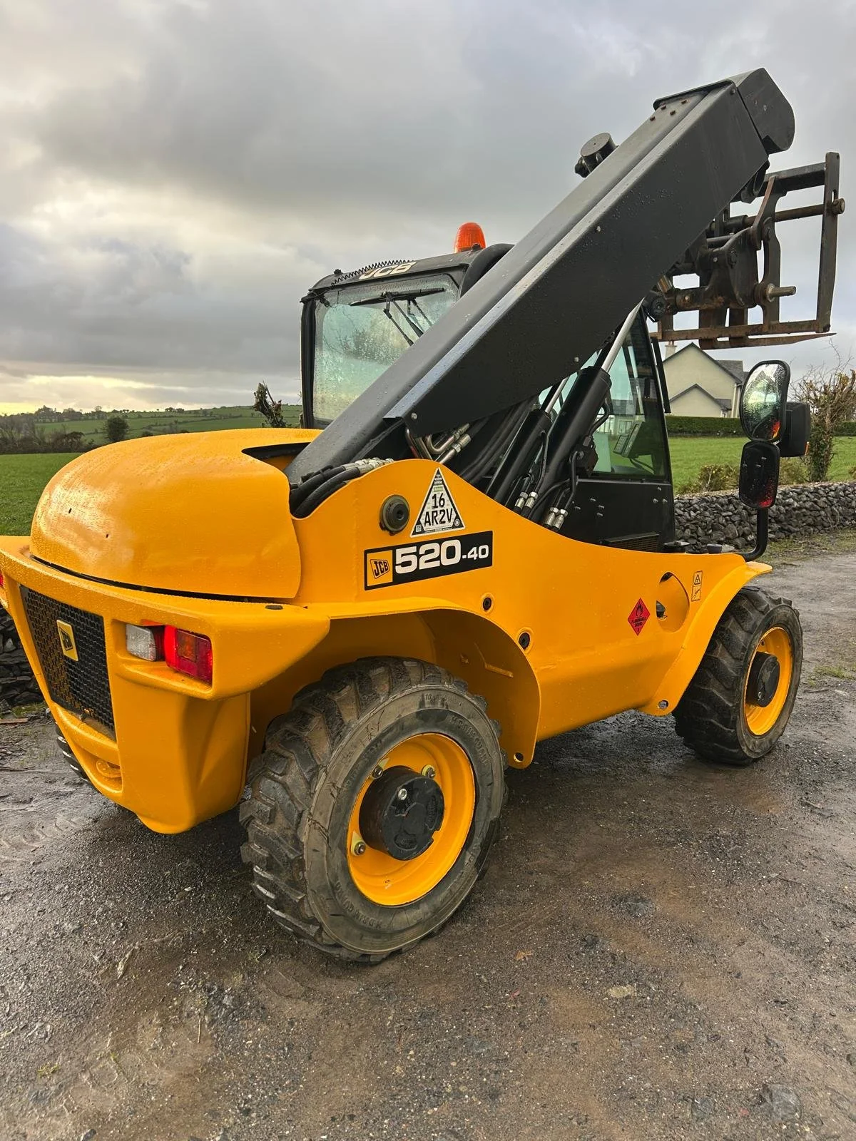 Yellow JCB 520-40 telescopic forklift on a dirt and gravel surface outdoors, with a cloudy sky and rural landscape in background.