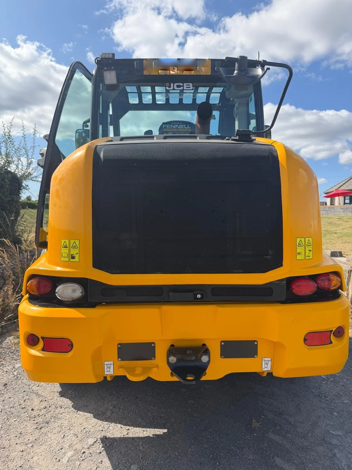 Front view of a yellow construction vehicle, likely a compact excavator, with safety stickers on the rear and a cloudy sky in the background.