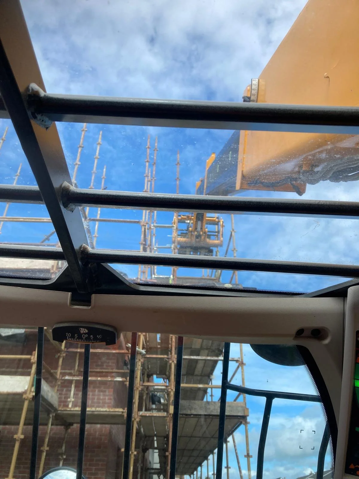 Construction site viewed from inside a vehicle, looking up at scaffolding and building structures against a blue sky.