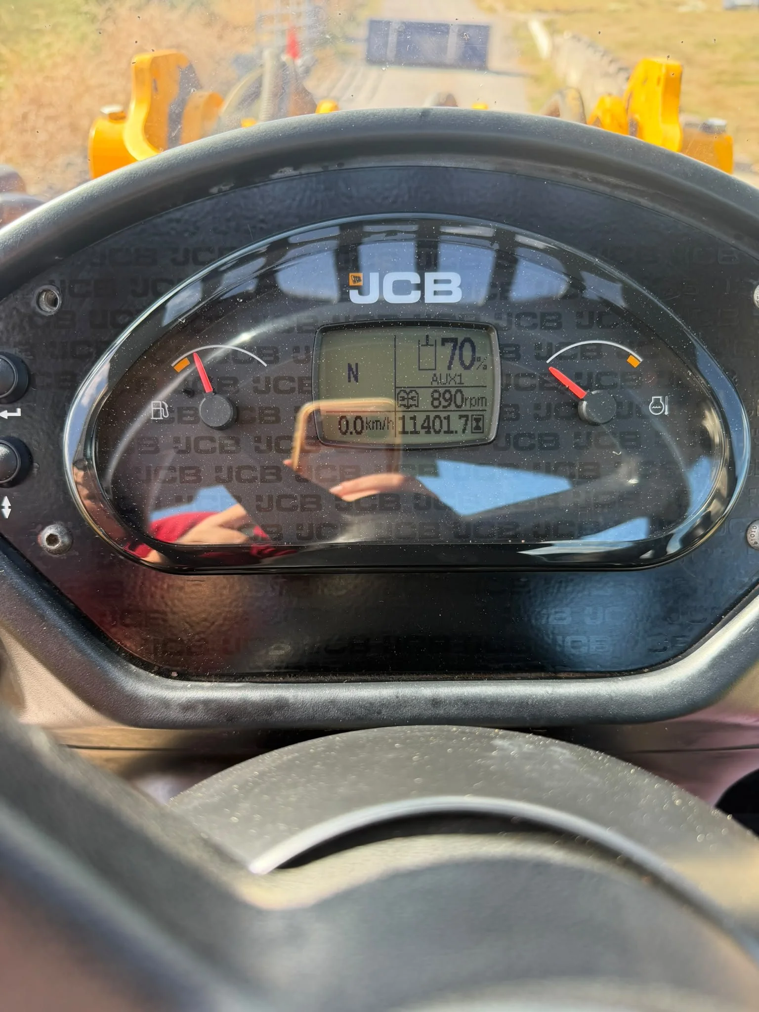 The image shows the dashboard of a JCB tractor, with the speedometer at zero, a digital display showing 11,401.7 hours and 70% battery, and the fuel gauge indicating a nearly full tank. The background includes parts of the tractor's yellow machinery 