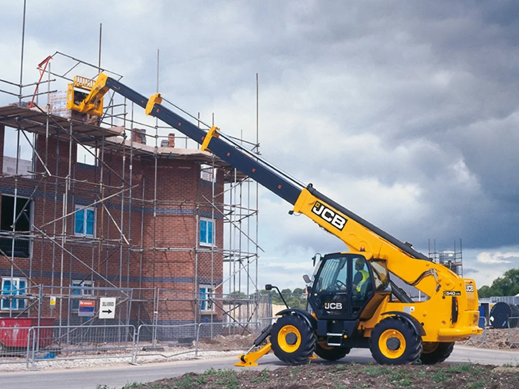 A JCB telescopic handler lifting construction materials on a building site with scaffolding around a brick building under cloudy sky.