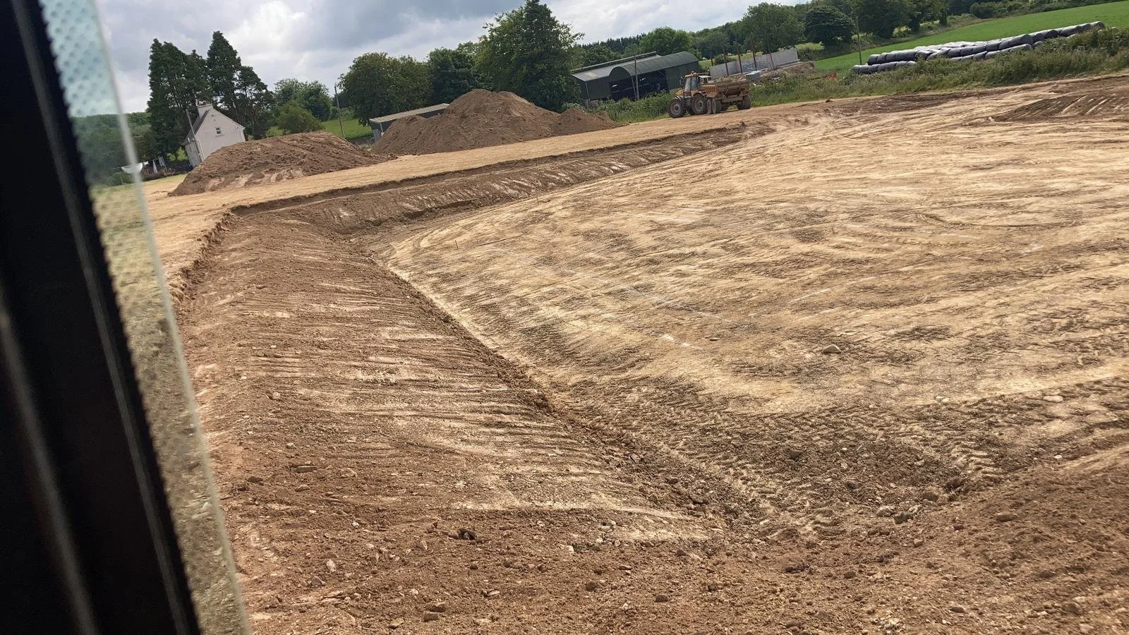A construction site with dirt and gravel, piles of earth, and construction equipment in the background.