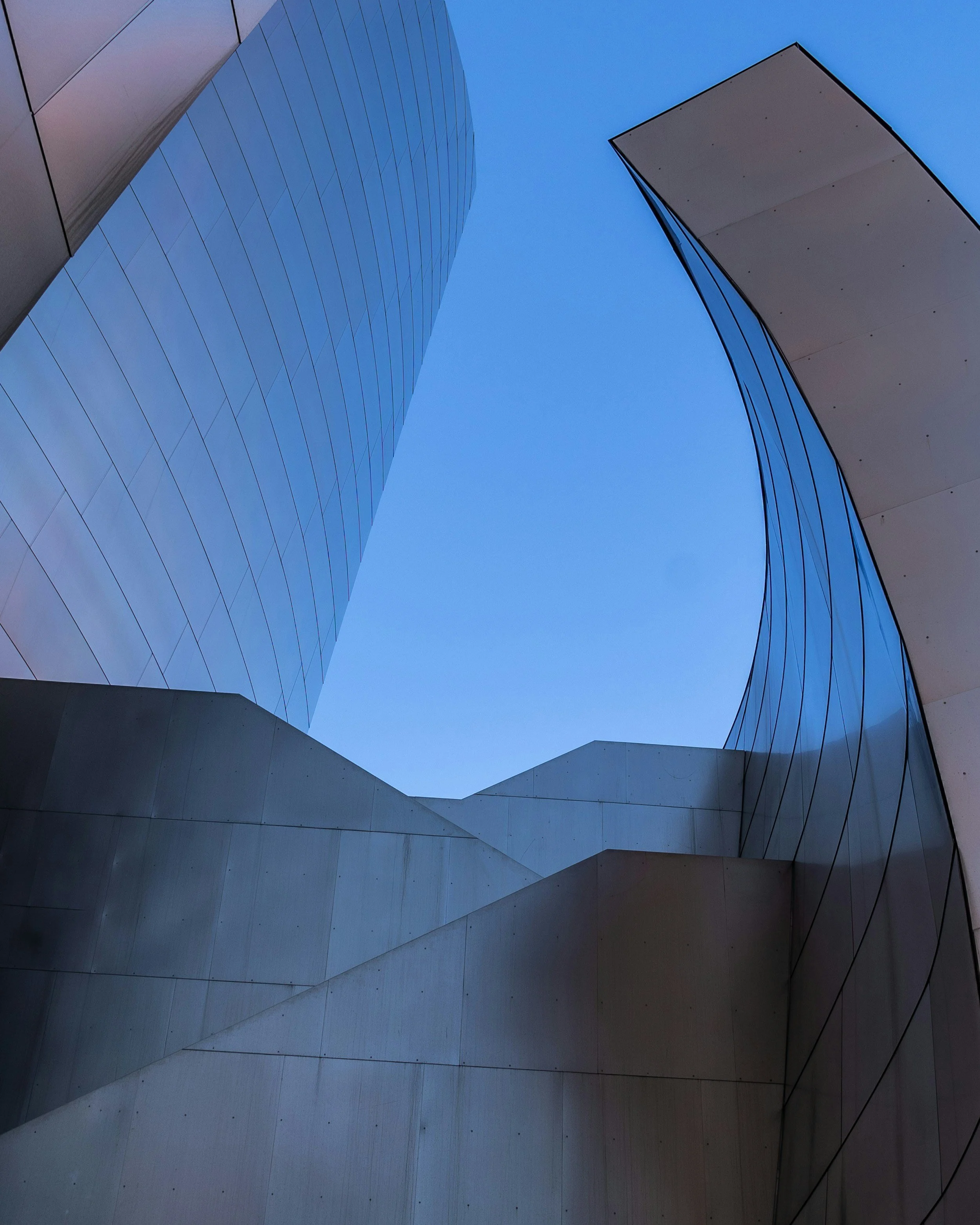 Low-angle view of modern glass and concrete buildings with curved and angular architecture against a clear blue sky.