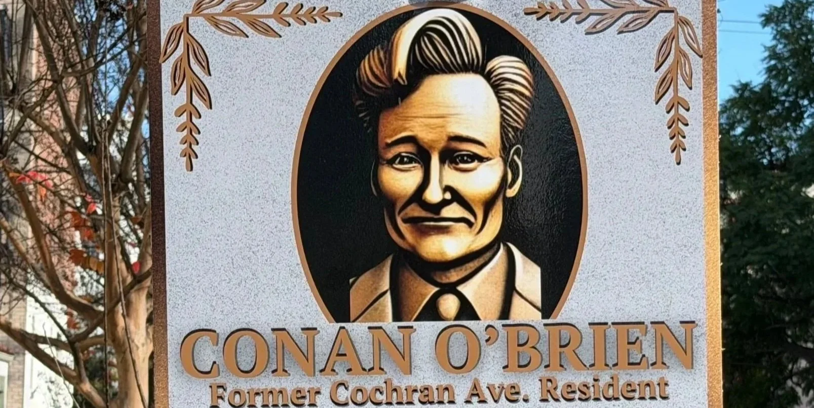 A sign with a portrait of a man, identified as Conan O'Brien, a former resident of Cochran Avenue. The sign has decorative leaves and text.
