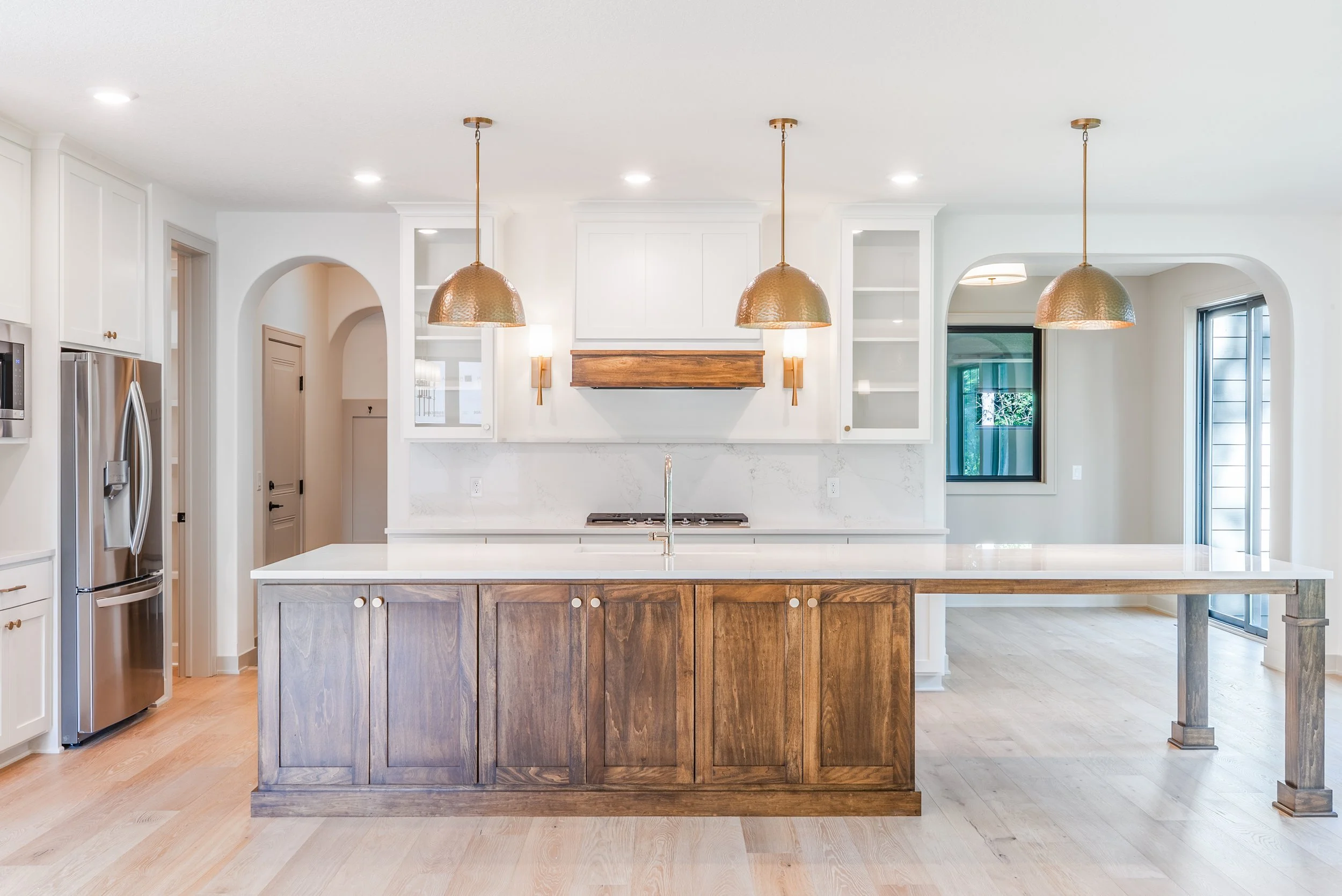 Modern kitchen with white cabinets, wooden island, pendant lights, stainless steel refrigerator, and light wood flooring.