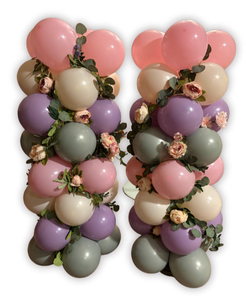 Two balloon columns decorated with pink, cream, purple, and green balloons, interwoven with pink and cream roses and greenery.