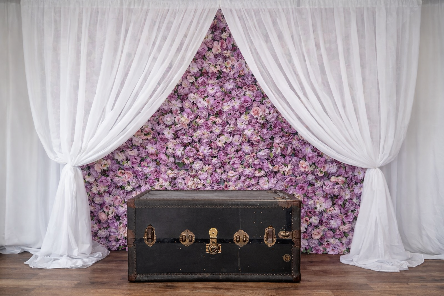 Vintage black trunk in front of a floral backdrop with pink and purple flowers and white curtains.