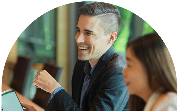 A man with short, styled hair smiling and interacting with others in a professional setting, likely an office or meeting room.