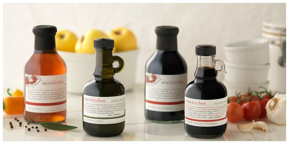 Label design and artwork for Mia's Kitchen brand, tomatoes, garlic, and a bowl of apples on a kitchen countertop.