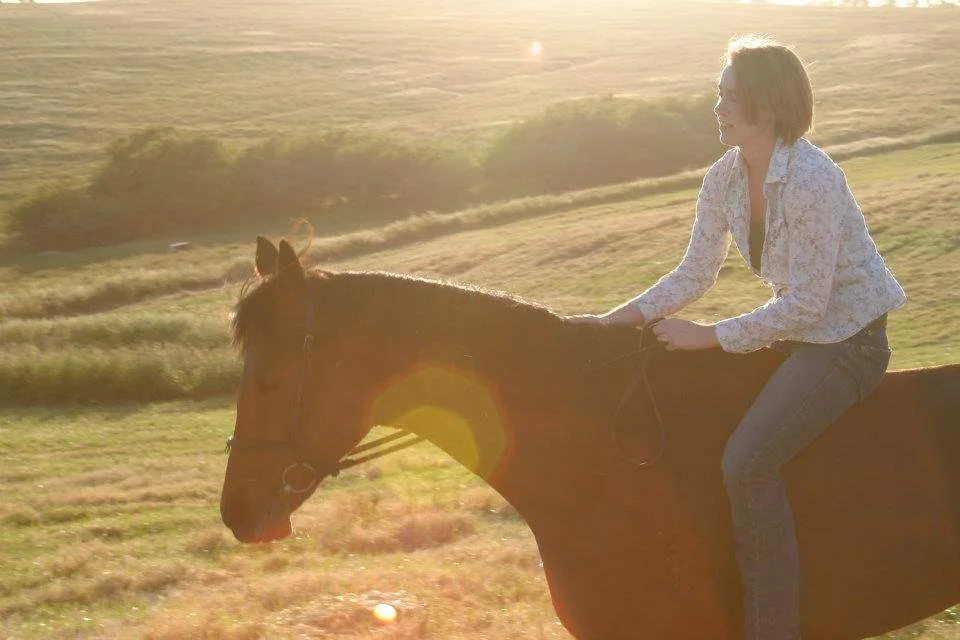 A woman riding a horse on a grassy field during sunset.