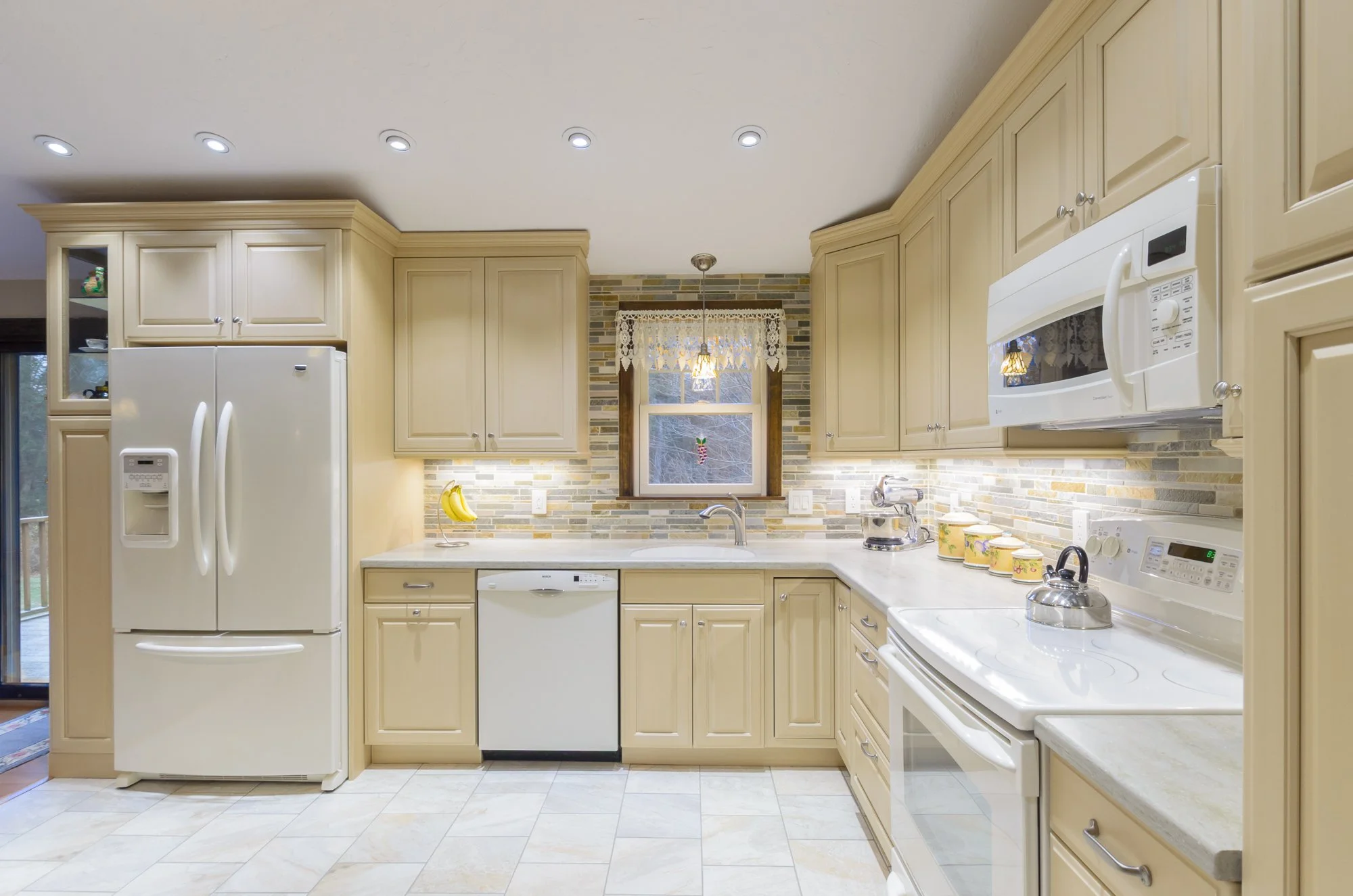 Kitchen with beige cabinets, white appliances, a window above the sink, and a tiled backsplash. Rooms With A View Tile