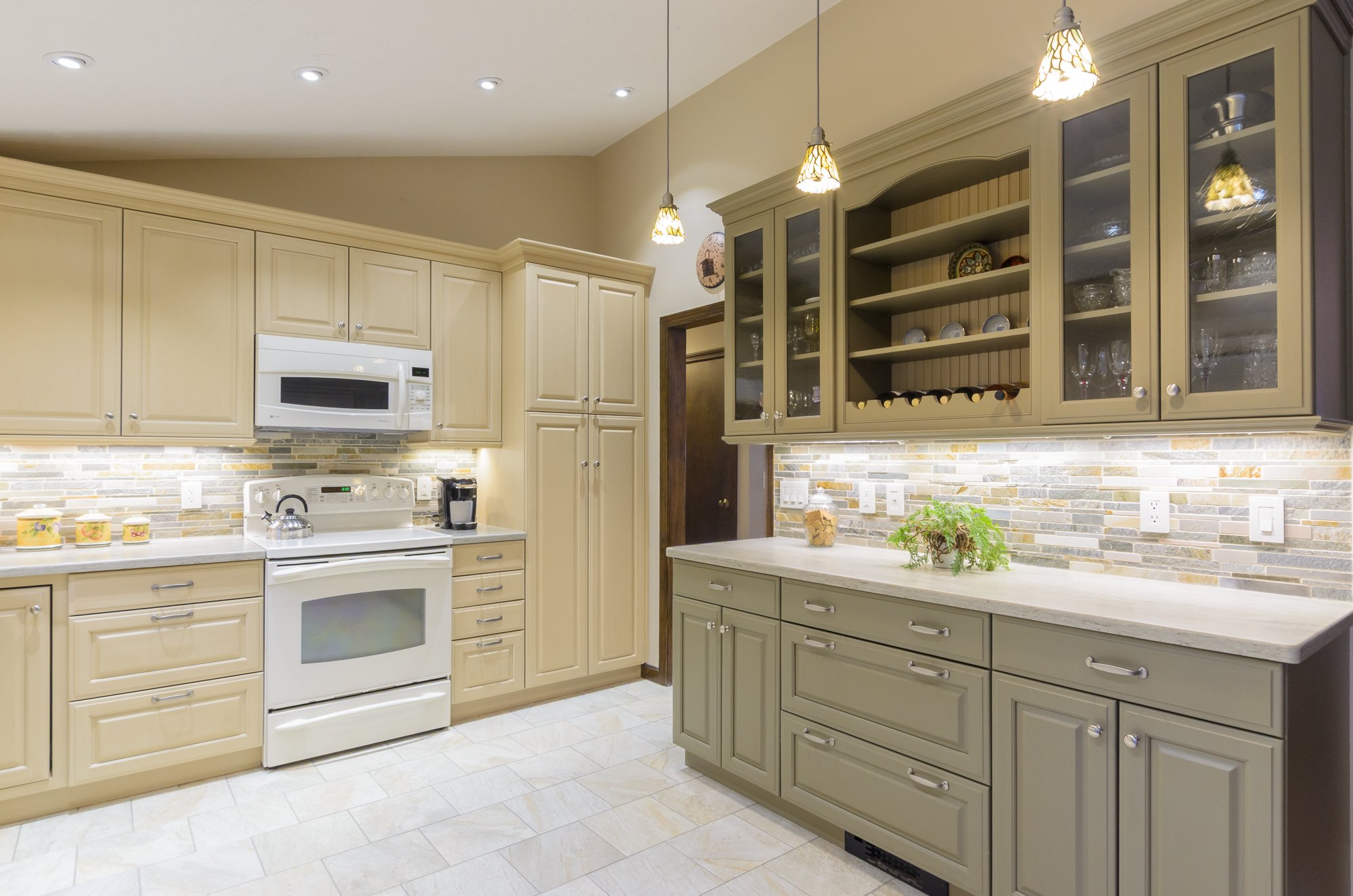 Kitchen with cream-colored cabinets, a white stove, microwave, and coffee maker, and a backsplash of multi-colored tile. Rooms With A View Tile