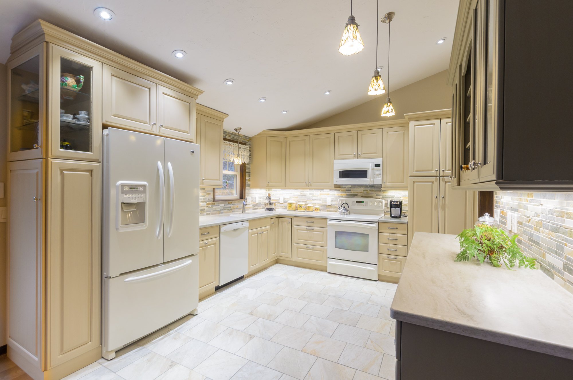 Bright kitchen with beige cabinets, white appliances, pendant lights, and a tiled backsplash. Rooms With A View Tile