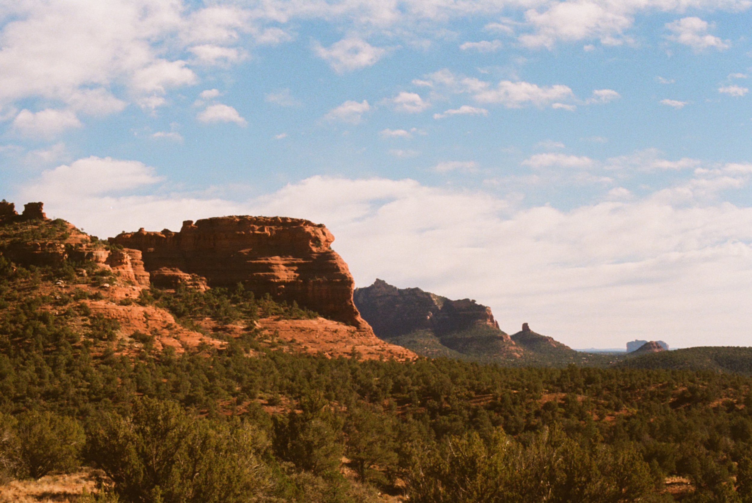Mountain range with red rock formations and sparse green vegetation under a partly cloudy sky