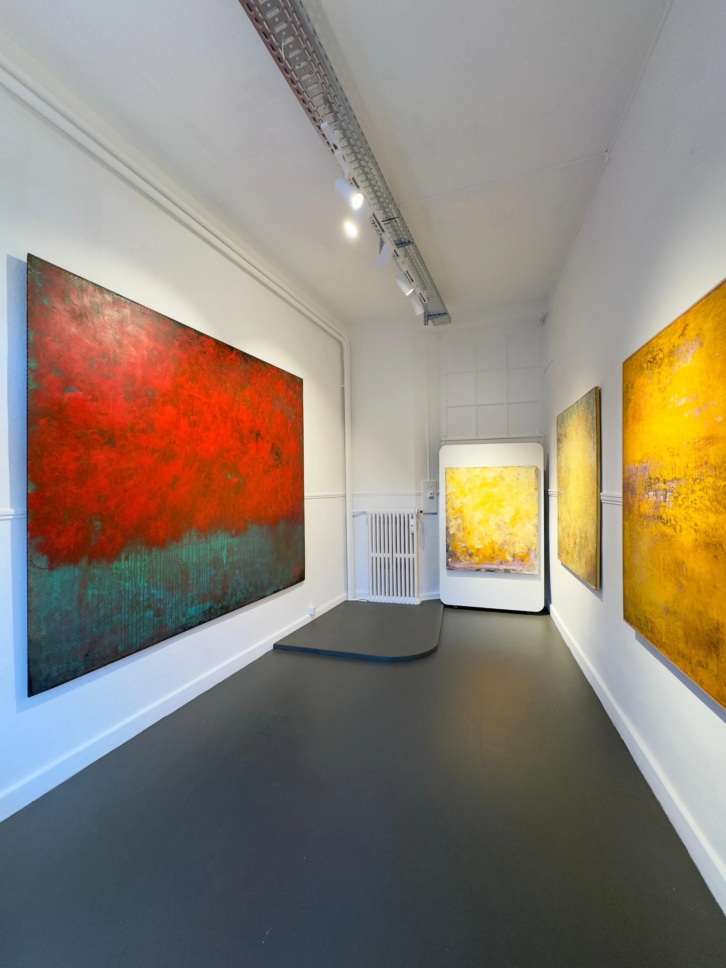 zeitgenössische Kunstgalerie in Baden mit vier großflächigen, farbenfrohen abstrakten Gemälden an weißen Wänden, Beleuchtung an der Decke und einem kleinen Podest in der Ecke.