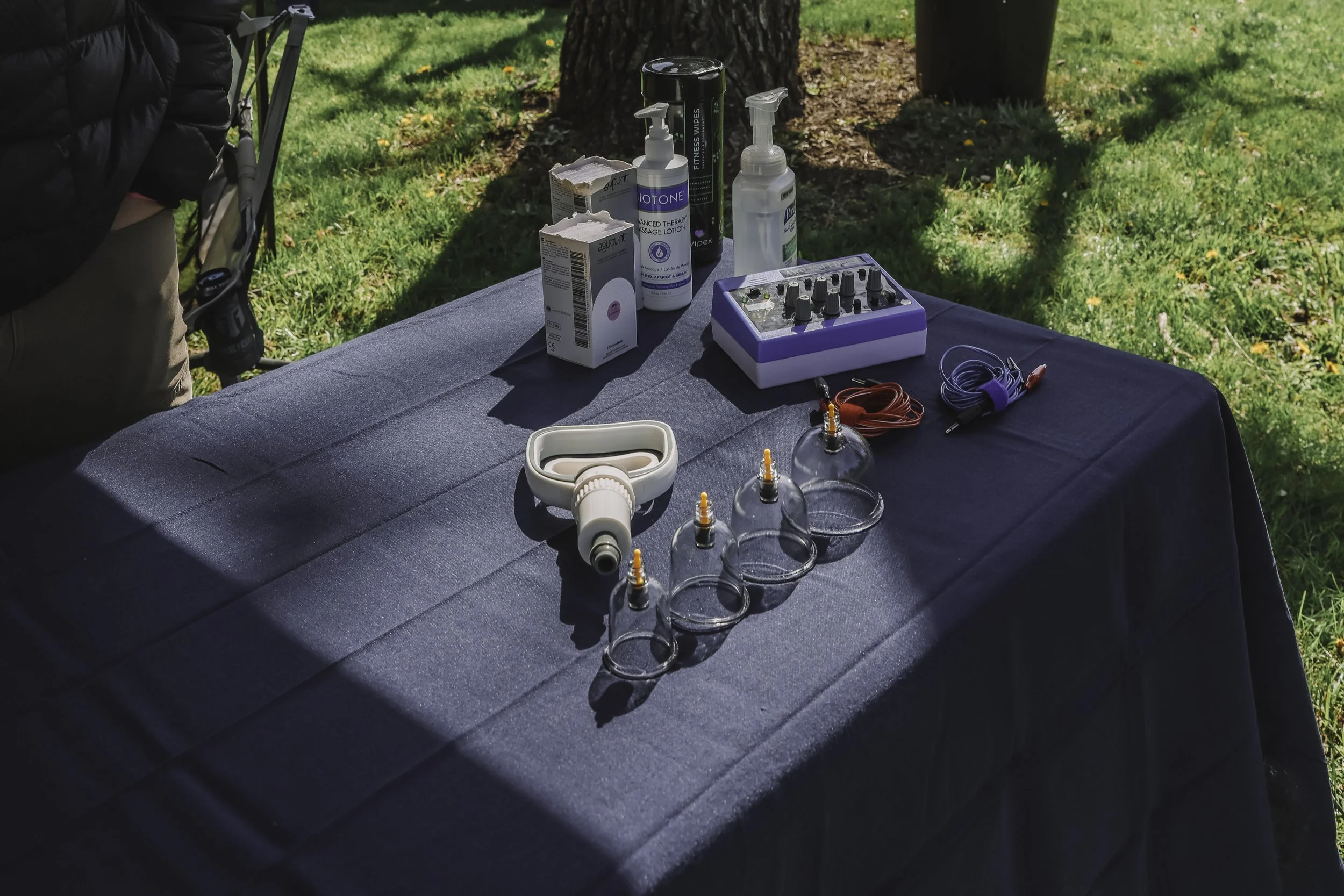 Outdoor table with medical supplies including vials, syringes, a nasal spray, bottles, and a small electronic device, set against a grassy area with trees.