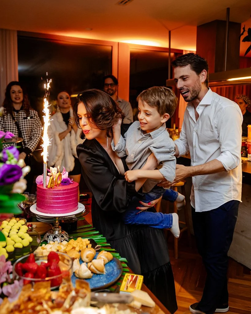 Família celebrando aniversário com bolo rosa, fogos de artifício e pessoas sorridentes ao redor.