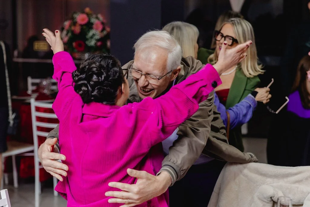 duas pessoas sorrindo e se abraçando em um ambiente social