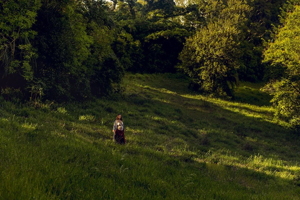 Pessoa caminhando em um campo verde rodeado de árvores sob luz do pôr do sol.