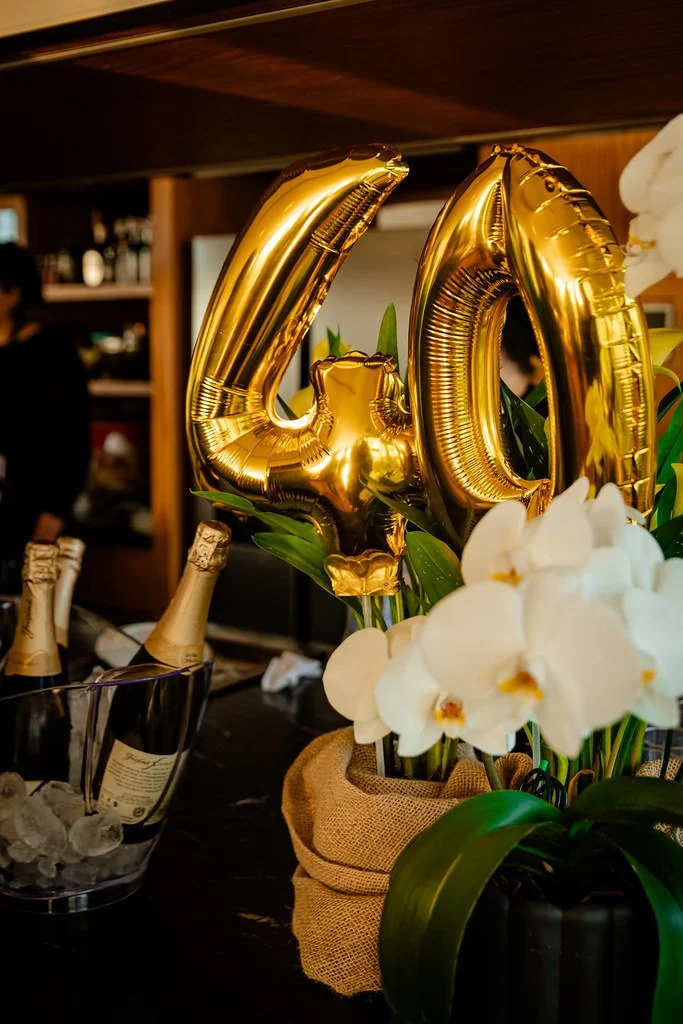 Balões dourados em formato de números 4 e 0, com flores brancas ao redor, decorando uma mesa em uma celebração.