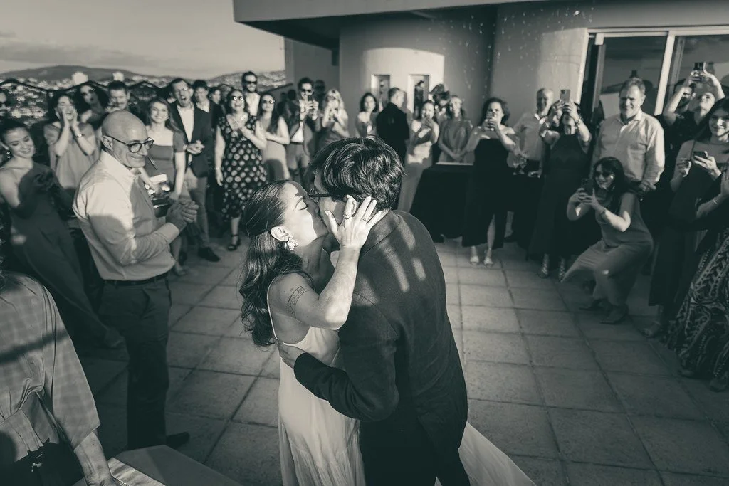 Casal se beijando em uma festa ao ar livre com muitos convidados assistindo.