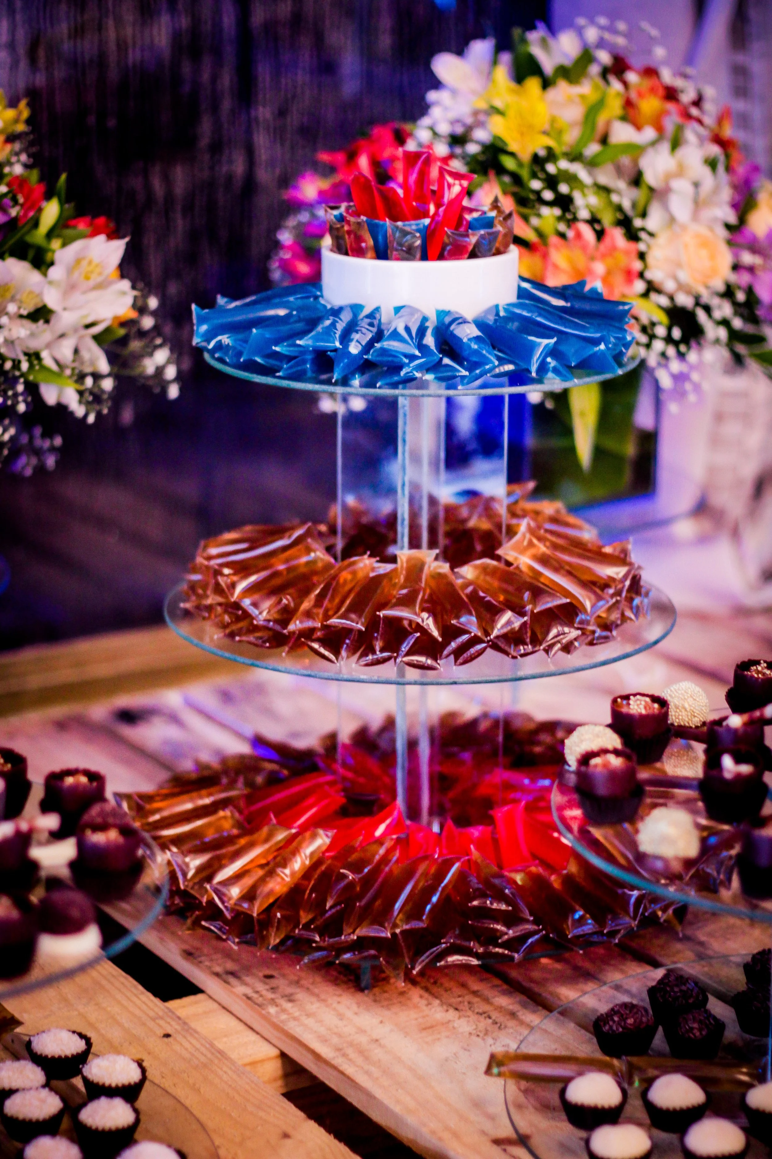 Mesa com várias guloseimas de chocolates e doces em camadas, decorada com flores ao fundo.