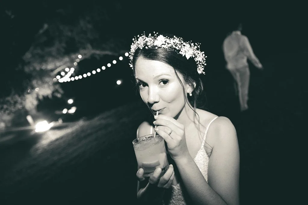Jovem mulher vestida de casamento com coroa de flores, tomando drink ao ar livre à noite