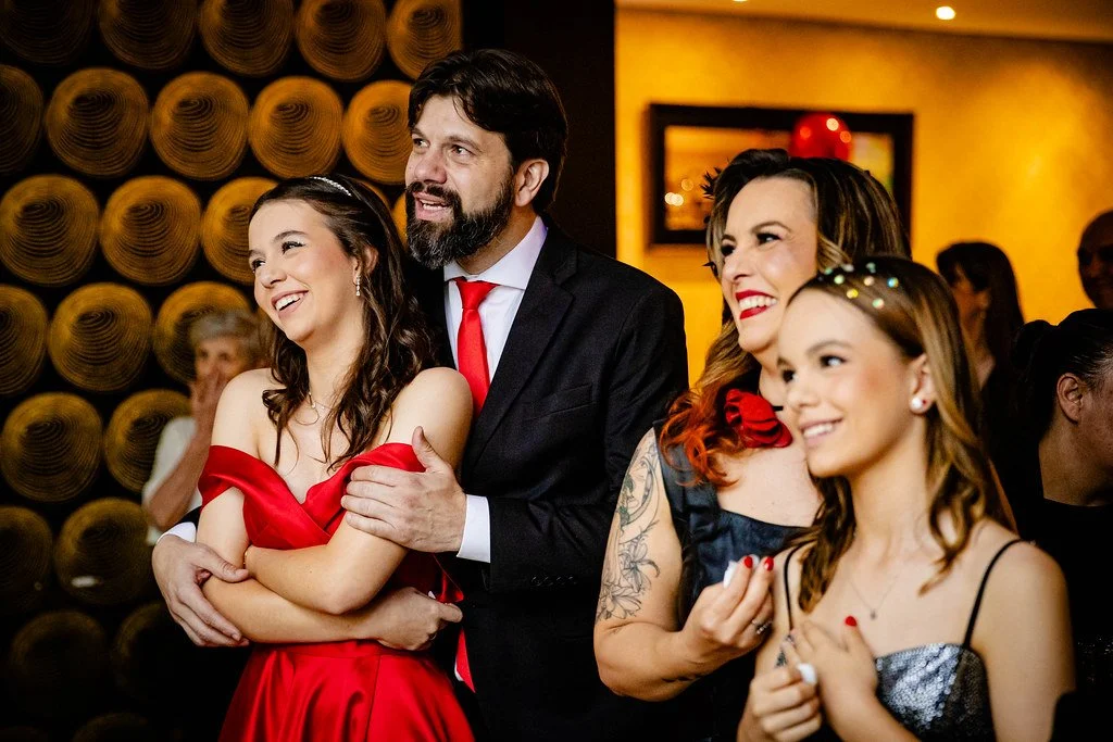 Grupo de pessoas felizes, incluindo duas mulheres, um homem e uma jovem, sorrindo e apreciando o momento em um ambiente interno, possivelmente uma celebração ou evento social.