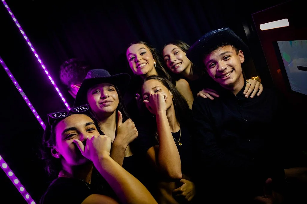 Grupo de jovens sorrindo e se divertindo em uma festa, com iluminação neon roxa ao fundo.