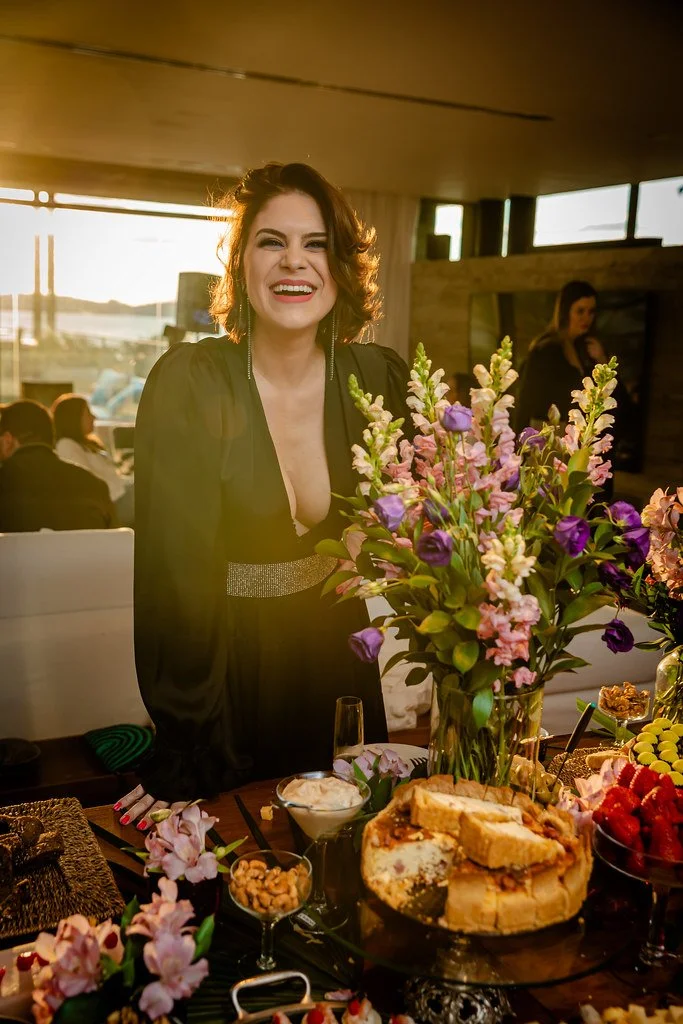Mulher sorrindo ao lado de mesa com flores e comida em celebração