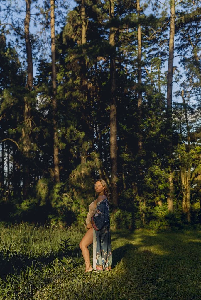 Mulher com vestido de banho e kimono fluido posando na floresta ao entardecer.