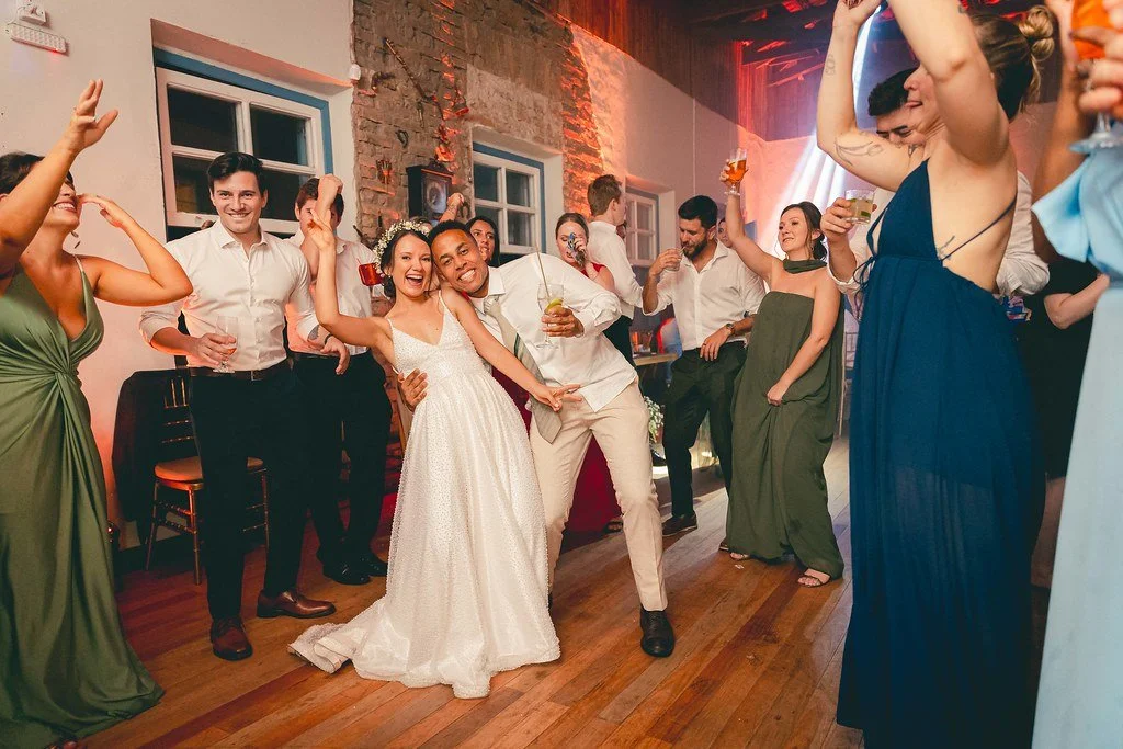 Pessoas celebrando uma festa de casamento com dança e brindes em um ambiente interno.