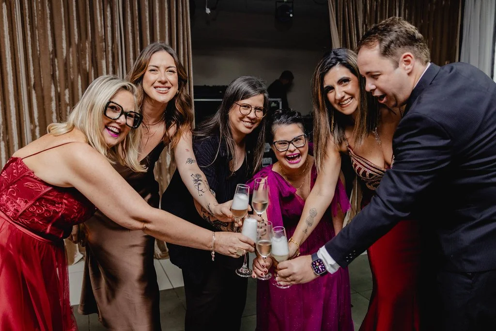 Grupo de seis pessoas comemorando, brindando com taças de champagne em um ambiente festivo.