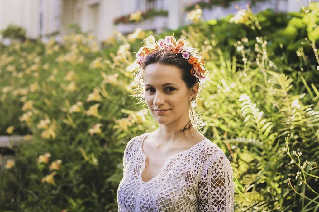 Jovem com flores no cabelo posando ao ar livre com folhagem ao fundo.