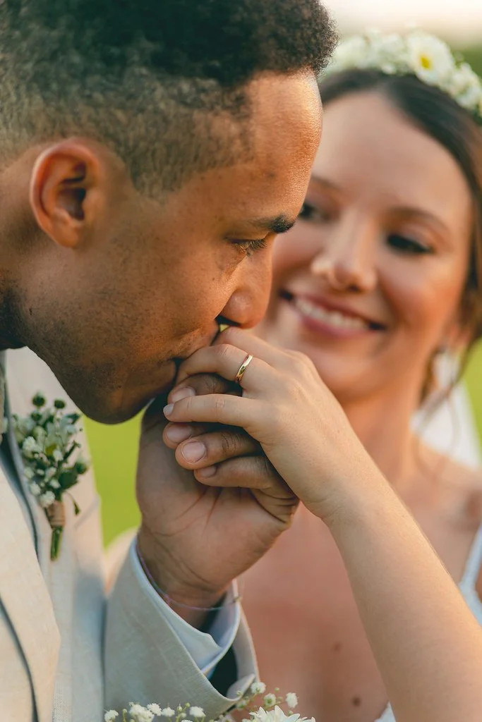 Homem beijando a mão de uma mulher sorridente, em um momento romântico ao ar livre.