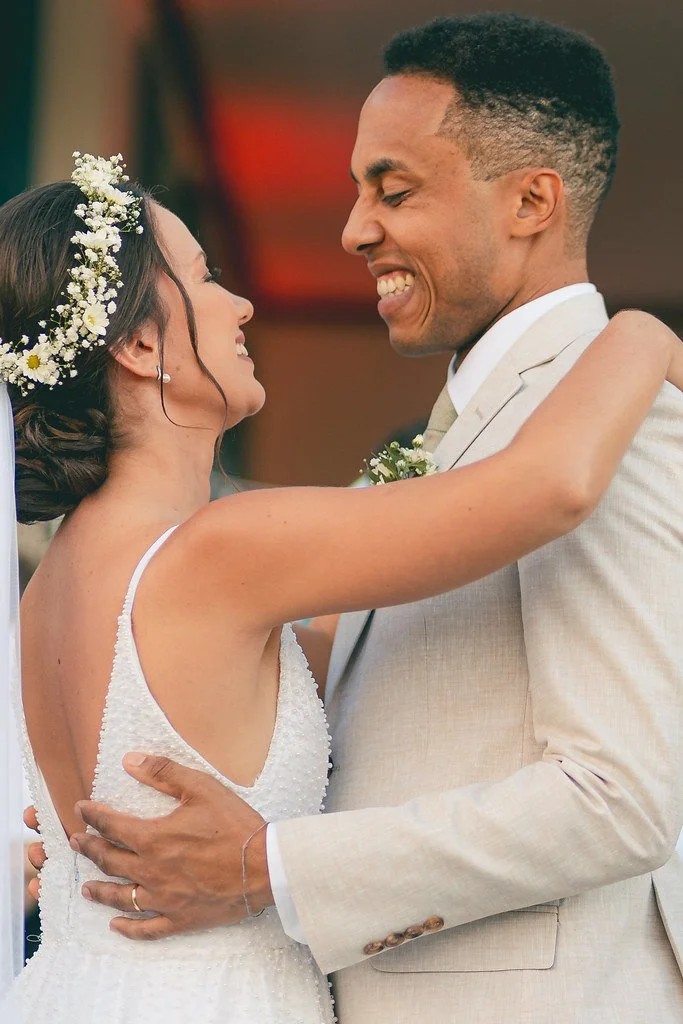 Casal de noivos sorrindo e se abraçando em um casamento.