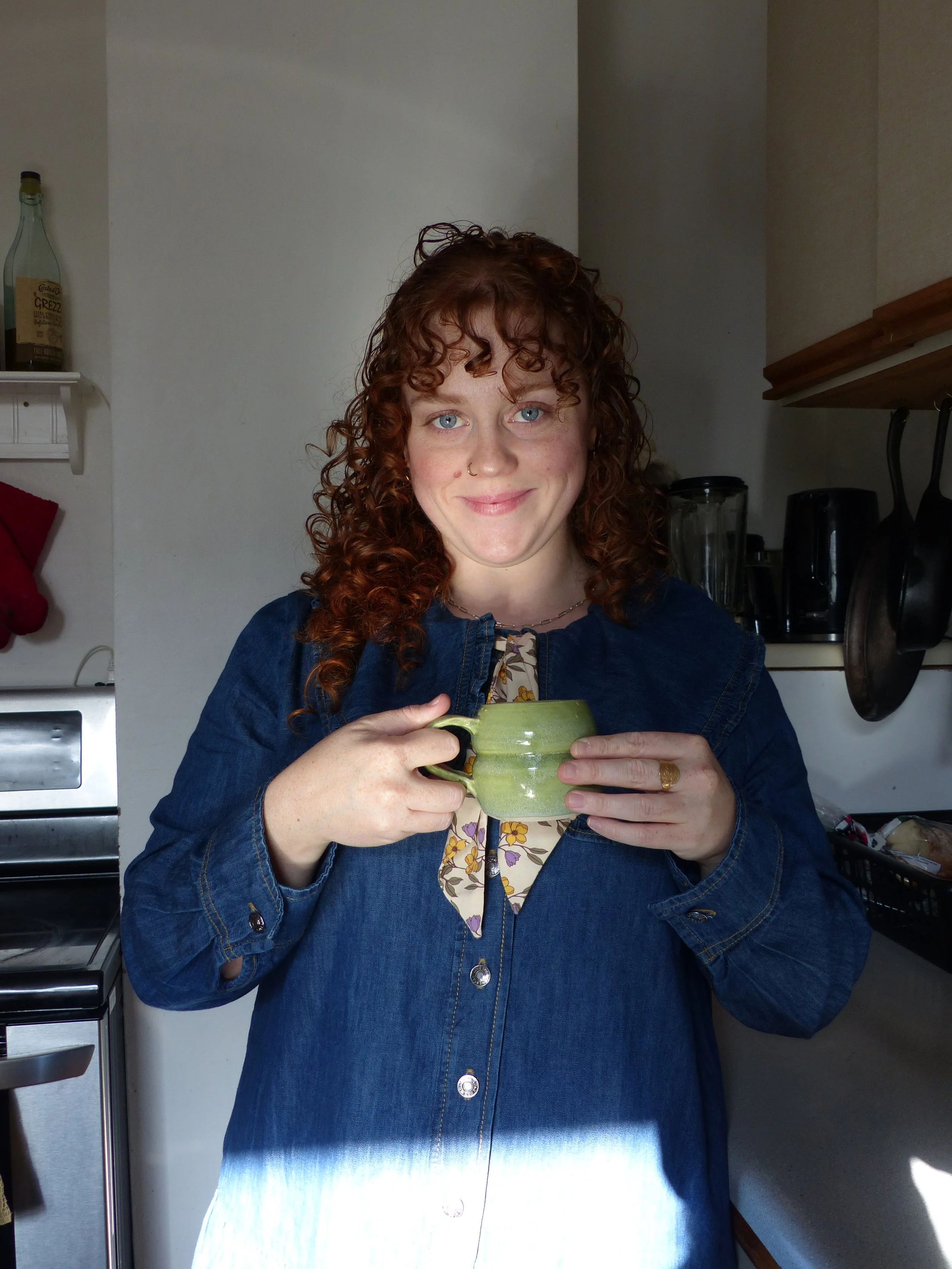 A woman with curly red hair holding a green mug in a kitchen.