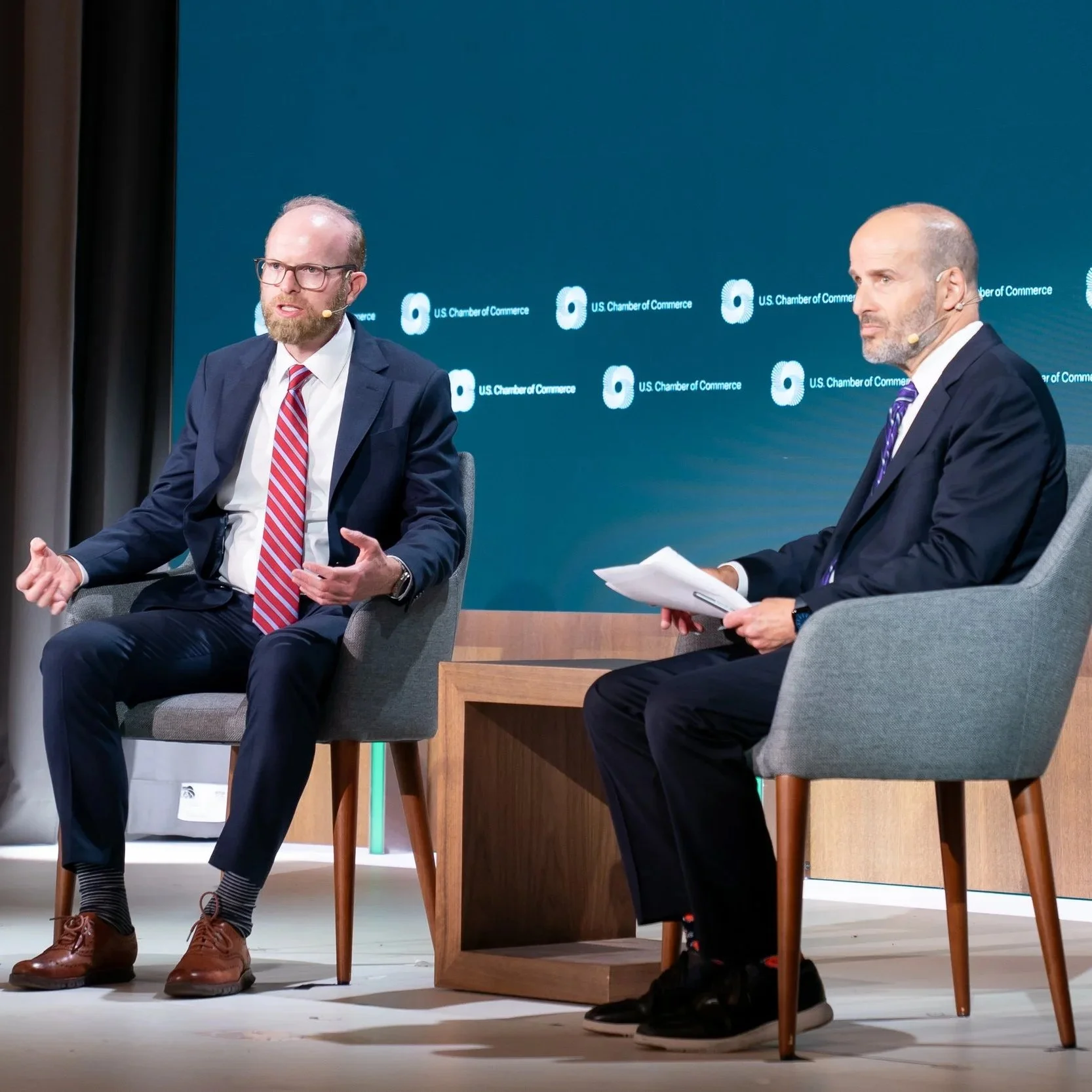 Daniel Kaniewski is having a discussion with a colleague at the U.S. Chamber of Commerce, with a blue background displaying the organization's logo.