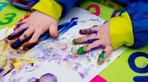 Child's hands with painted fingers pressing on paper with colorful paint strokes.