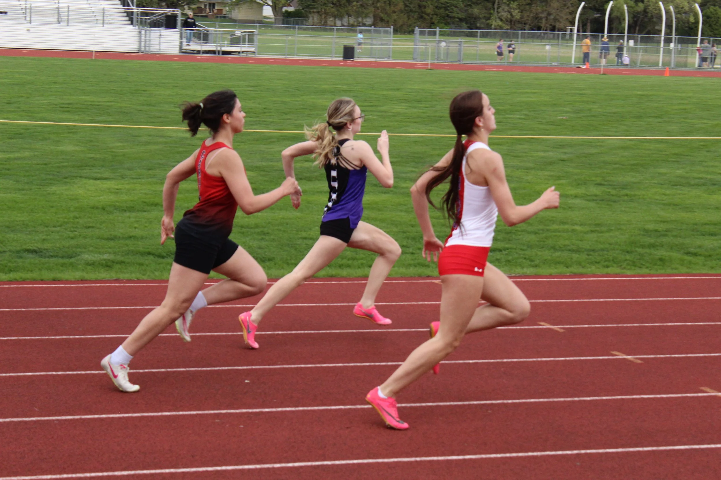 Three women running on a track at an outdoor athletic stadium during daytime.