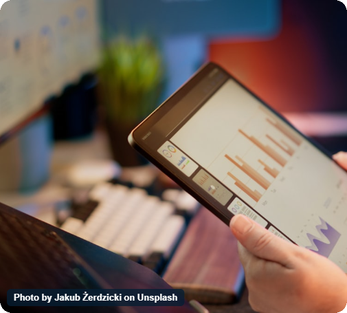 Person analyzing data on a tablet with bar graphs and charts in an office setting.