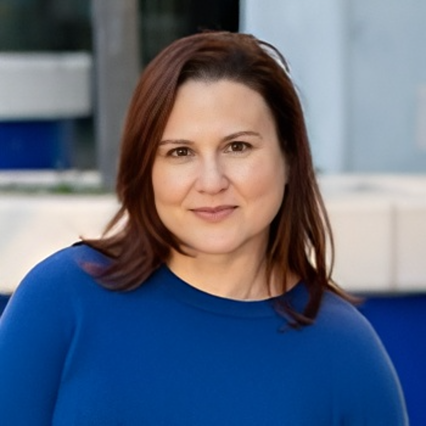 Portrait of a woman with shoulder-length brown hair wearing a blue top, smiling in an indoor setting.